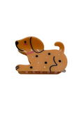 A dog-shaped hair clip in tan and brown with black details, displayed on a pink backing card with a bow illustration.