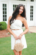 Woman in a white outfit holding a woven handbag outdoors.