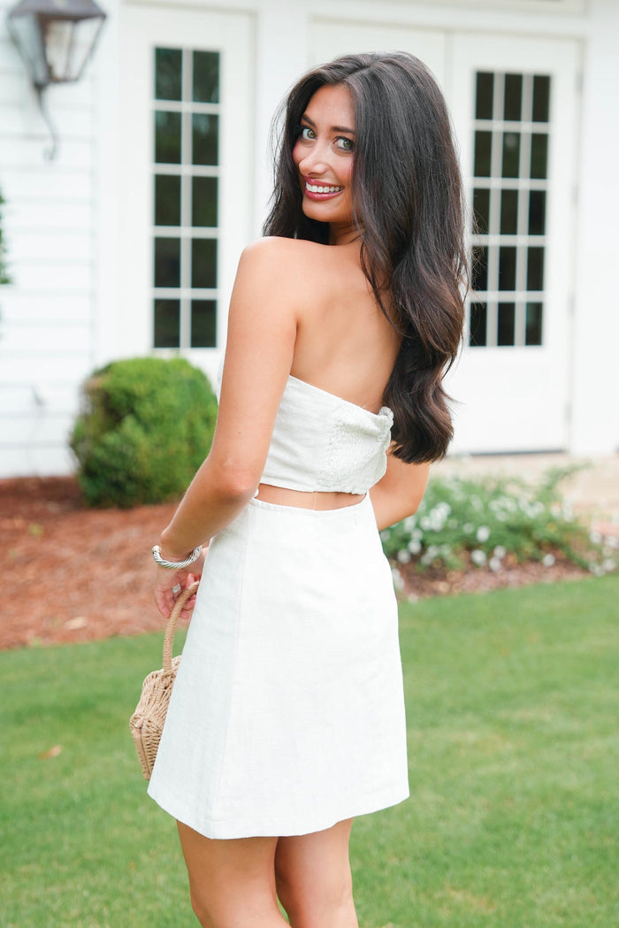 Woman in a white strapless top and skirt standing outdoors.