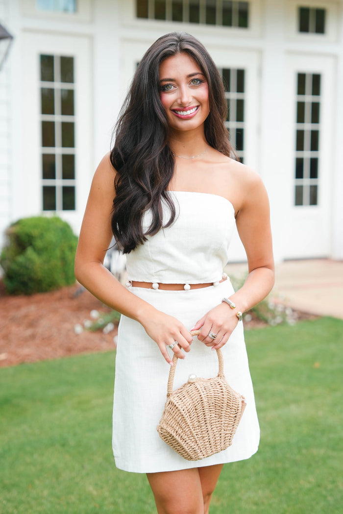 Woman in a white dress holding a straw bag outdoors.