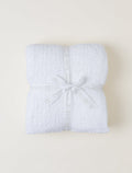 A folded white blanket wrapped with a white ribbon printed with the brand name 'BAREFOOT', tied in a bow, on a light beige background.
