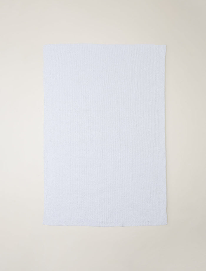A light textured blanket laid flat against a neutral cream-colored background.