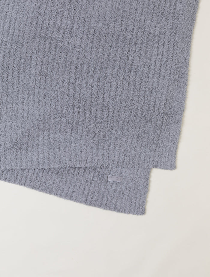 A close-up of a folded ribbed knit fabric in a muted dusty lavender-gray color, showing the soft texture and a small matching fabric tag, on a plain off-white background.