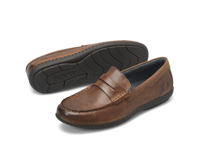 A pair of brown leather penny loafers, with one shoe showing the brown textured leather upper and the other showing the black treaded sole branded with 'Born'.