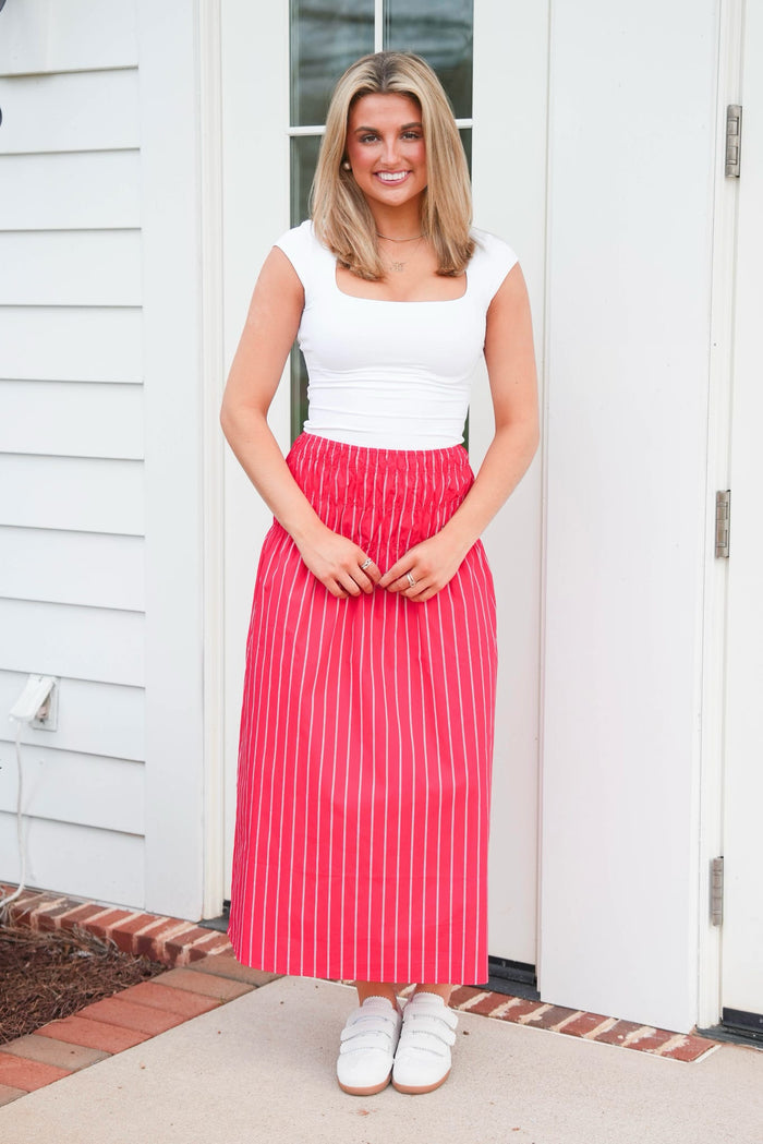 Woman wearing a white top and red striped skirt standing in front of a white door.