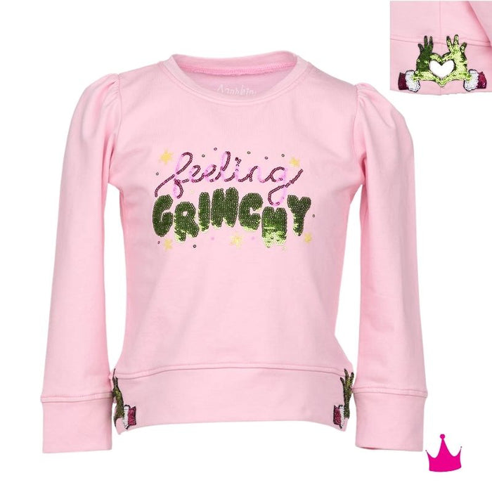 A pink long-sleeve sweatshirt for kids, featuring the phrase 'feeling GRINCHY' in glittery green and purple lettering on the front. The sweatshirt has puffed sleeves, ribbed cuffs, and a ribbed hem, with small green and pink character graphics near the lower hem.