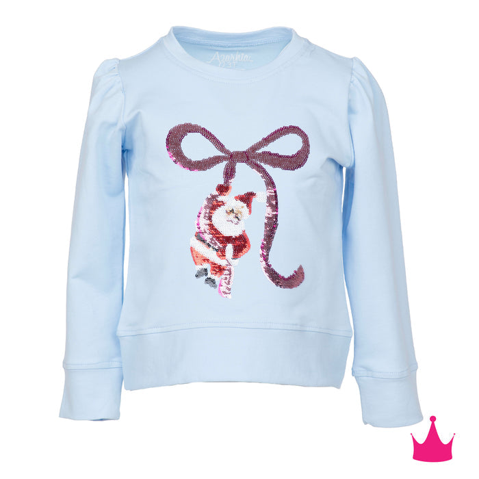 A light blue long-sleeve sweatshirt featuring a sequined graphic of a cat in a Santa outfit under a large sequined bow. The brand name 'Amigo' is visible on the inner neck label.