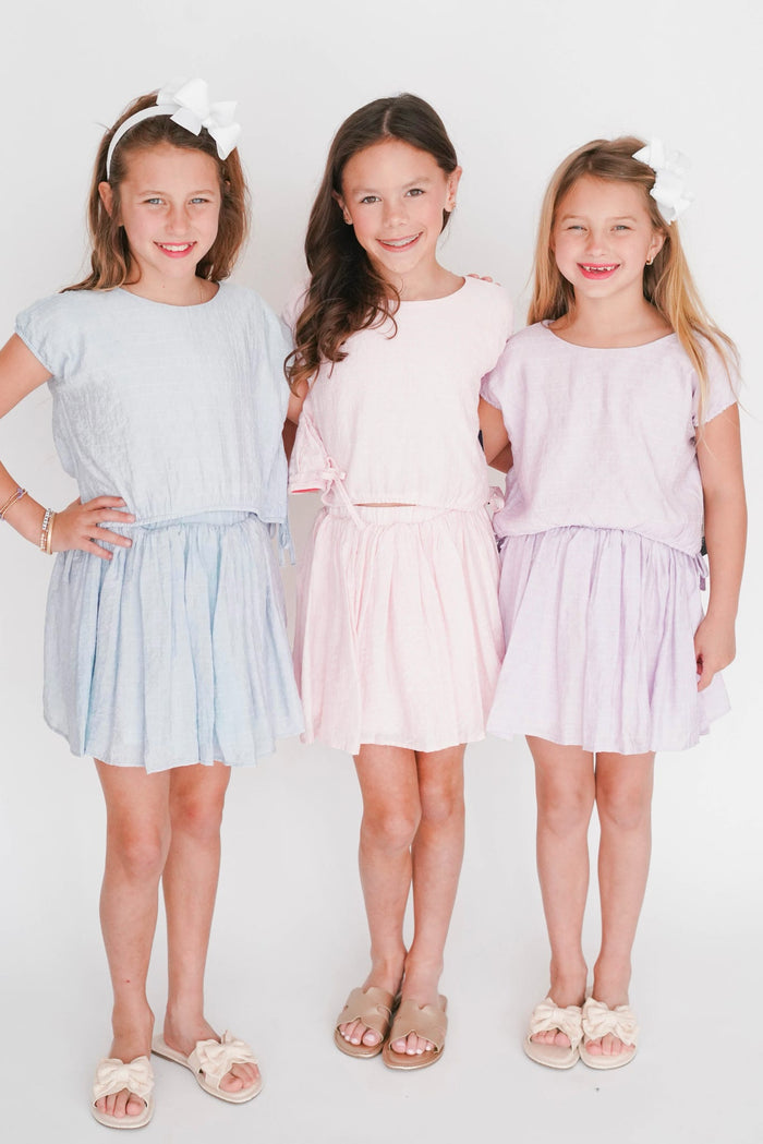 Three young girls wearing light-colored dresses standing against a white background