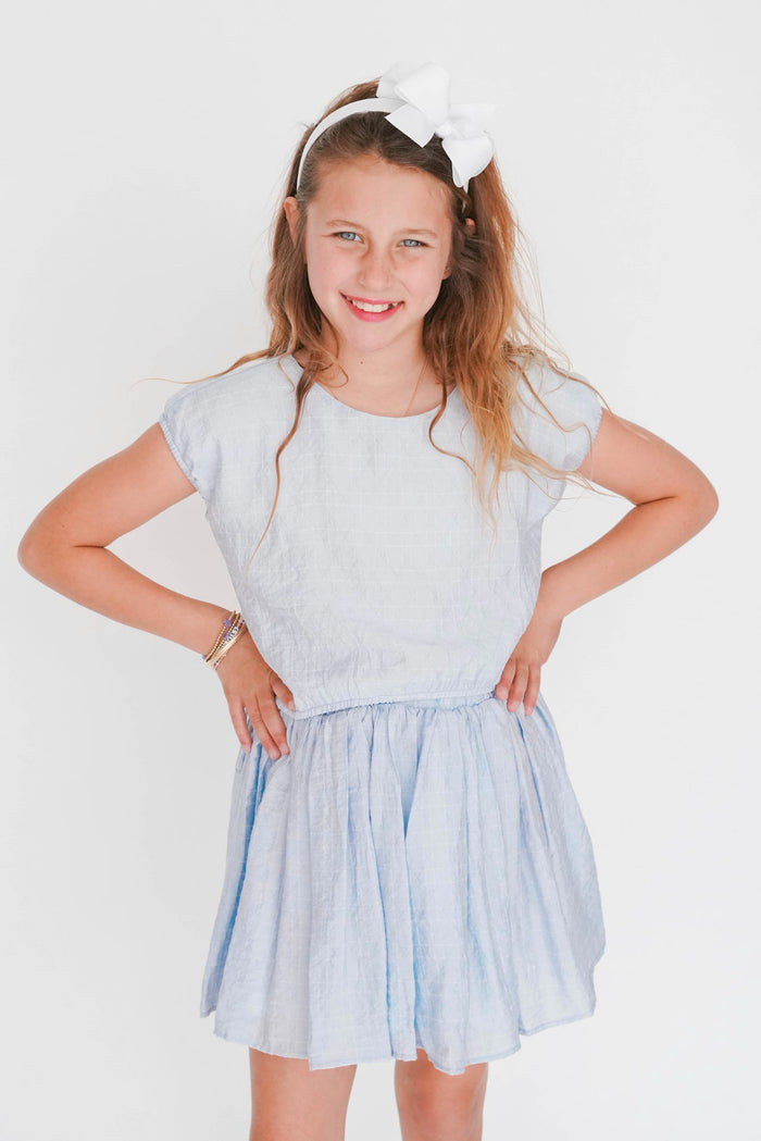 Young girl wearing a light blue dress with a white headband on a plain background