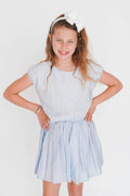 Young girl wearing a light blue dress with a white headband on a plain background