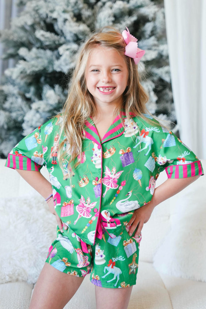 Young girl wearing a green pajama set with festive designs in front of a decorated Christmas tree.