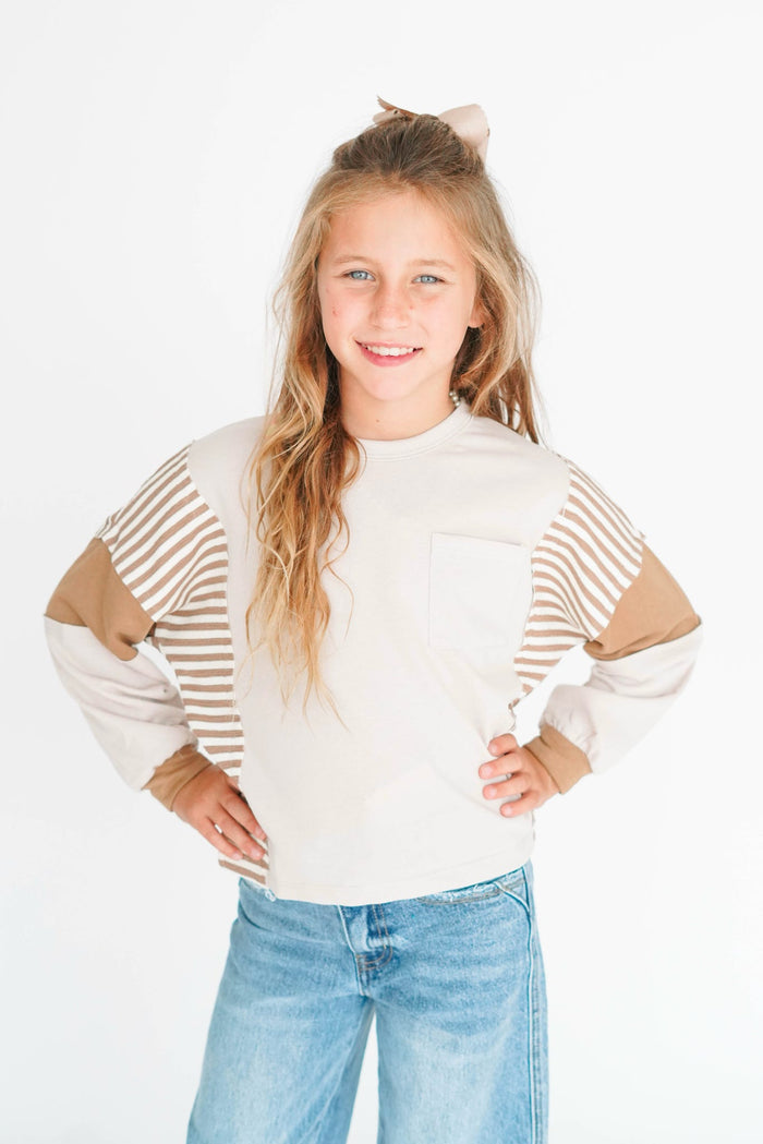 Young girl wearing a white and beige striped sweater with blue jeans on a white background