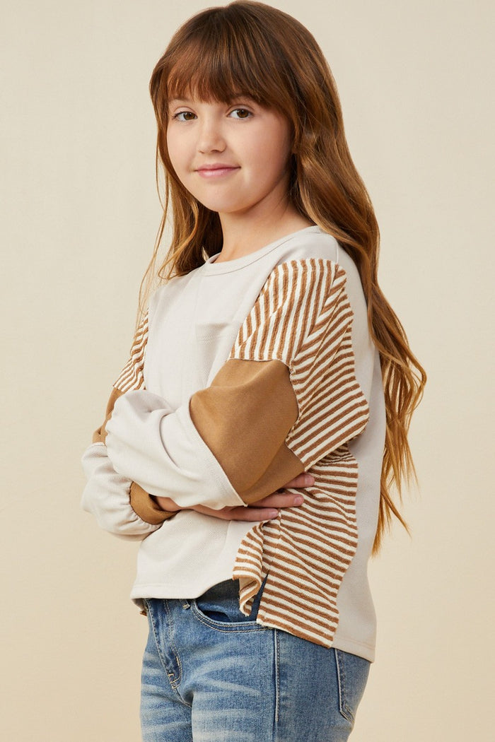 Young girl wearing a white and brown striped shirt with blue jeans on a beige background