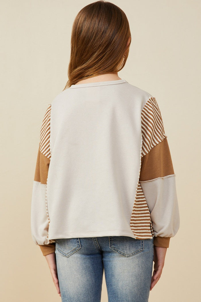 Person wearing a beige sweater with brown and striped sleeves on a beige background