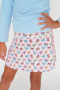 A child wearing a light blue long-sleeve top and a pink skirt with a colorful butterfly print, shown from the waist down against a plain white background.