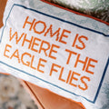 Cross-stitched pillow with 'Home is where the eagle flies' text.