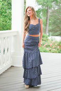 Woman wearing a navy polka dot dress on a wooden porch with greenery in the background