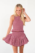 A blonde woman modeling a sleeveless red and white gingham mini dress with a smocked waist and ruffled skirt, set against a plain white studio background.