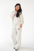 A woman modeling a matching light beige sweatshirt and sweatpants lounge set with red collegiate lettering that reads 'ALABAMA GAMEDAKS' on a plain white studio background.