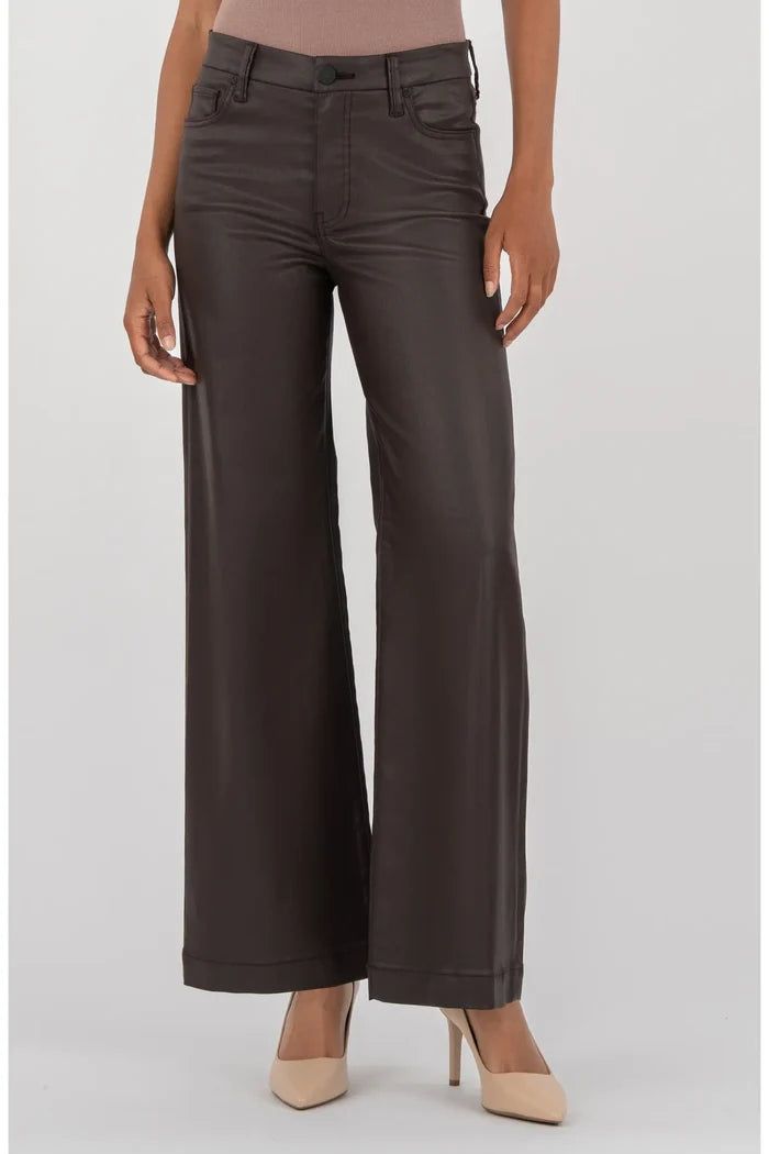 A model wearing dark brown wide-leg faux leather pants, paired with a dusty rose top and beige heels, against a light gray studio background.