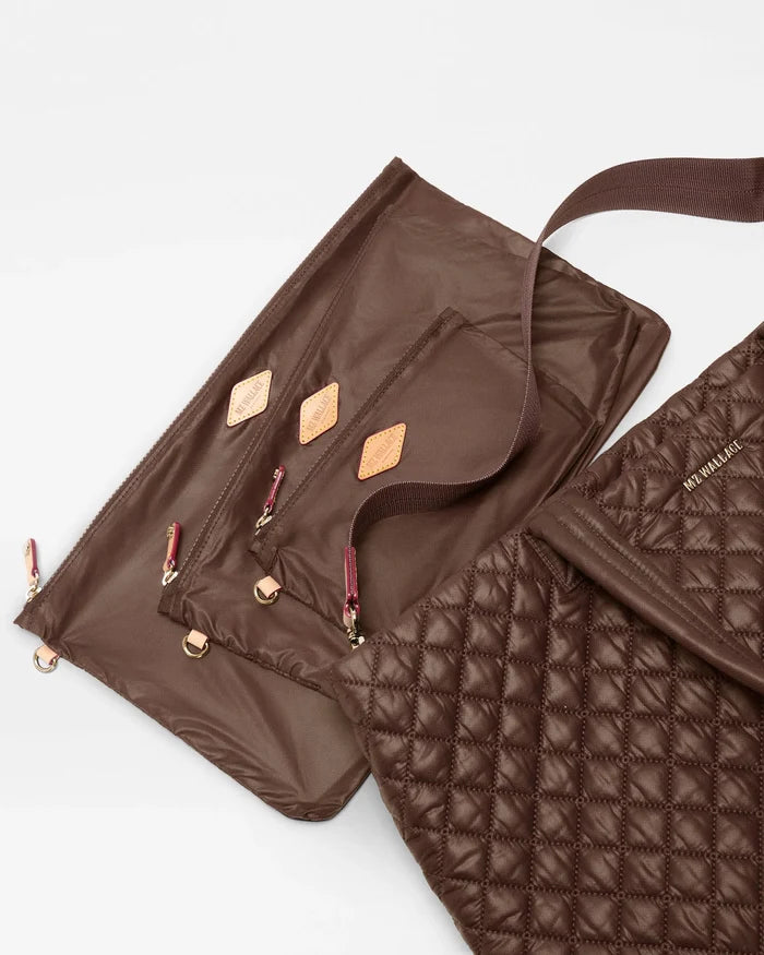 A close-up studio shot of a brown quilted puffer bag layered over a matching brown nylon pouch with multiple zippered pockets and tan leather accent tabs, on a light gray background.