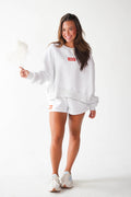A woman modeling a white sweatshirt and matching shorts set with orange box logo details, standing against a plain white studio background.
